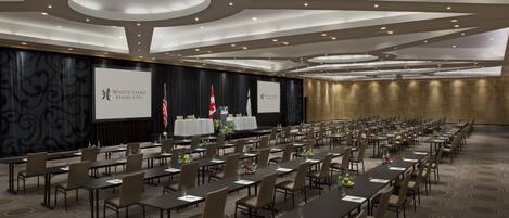 A conference room with multiple tables and chairs, a stage with a podium, and flags.