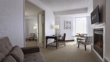 A hotel room with a sofa, a dining table with chairs, a TV mounted on the wall, and a fireplace.