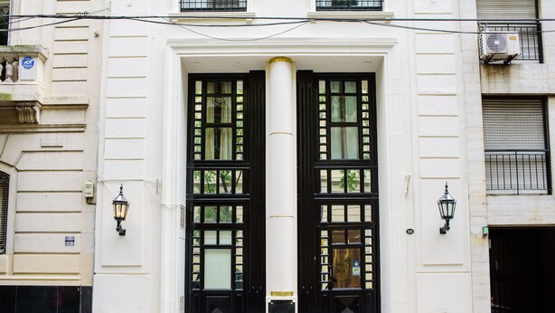 A building facade with a central entrance featuring two large black doors with glass panels, flanked by two black lantern-style lights, and a white column in the center. - 1253 Recoleta Small Hotel (Buenos Aires)