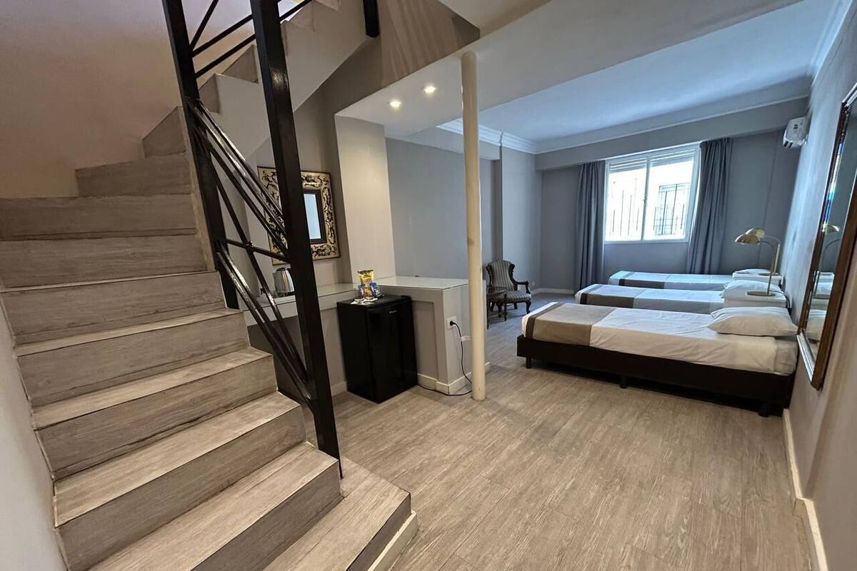 A modern hotel room with a wooden staircase, a bed, a desk, and a window with curtains.