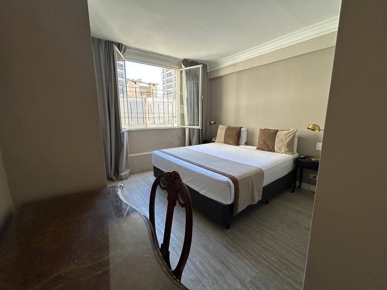 A hotel room with a large bed, a nightstand, a chair, and a window with curtains.