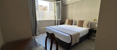 A hotel room with a large bed, a nightstand, a chair, and a window with curtains.