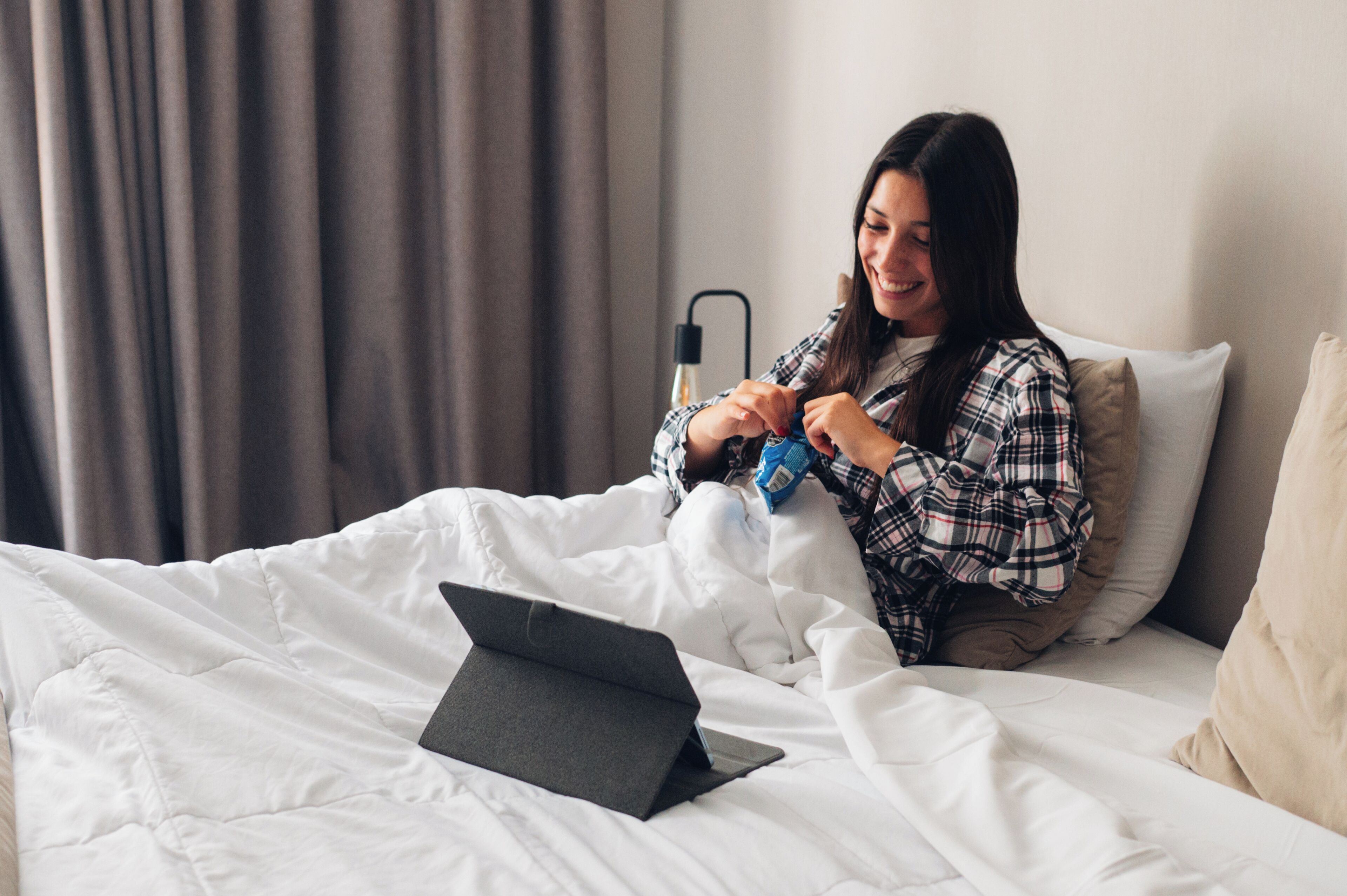 A person sitting on a bed with a laptop, a bottle, and a blanket.