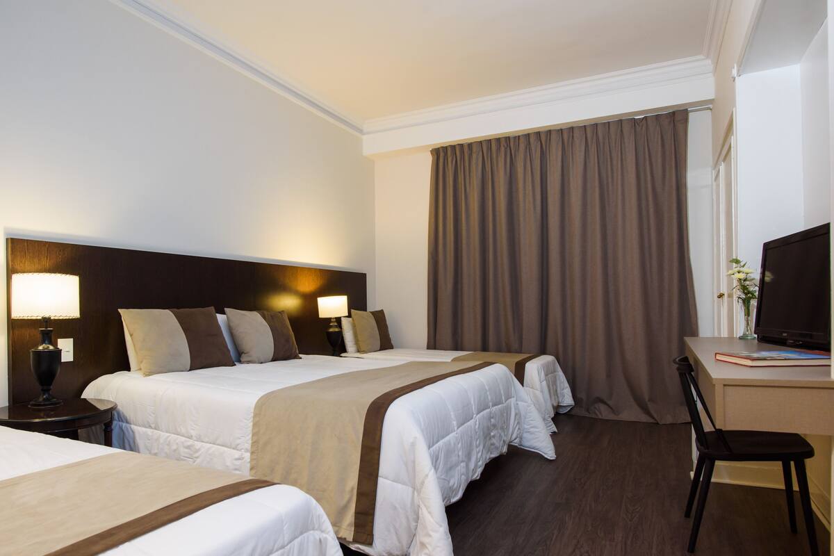 A hotel room with two beds, a desk, a chair, and a television.