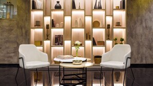 A modern interior with two white armchairs, a round table, and a wooden shelving unit with various decorative items. - 1253 Recoleta Small Hotel (Buenos Aires)