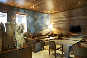 Un interior acogedor con pared de piedra, techo de madera, un sofá, sillones, una mesa y un televisor.