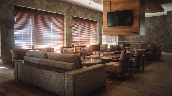 A spacious lobby with a stone wall, large windows with blinds, and a flat-screen TV mounted on the wall. - Radisson Hotel Puerto Varas (Puerto Varas)