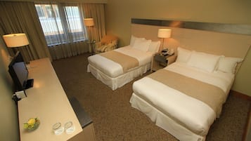 Habitación de hotel con dos camas, un escritorio, una silla y un televisor.