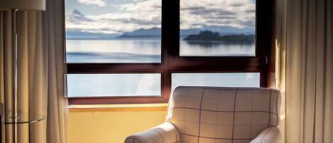 A room with a view of a lake and mountains through a window, a chair, and curtains.