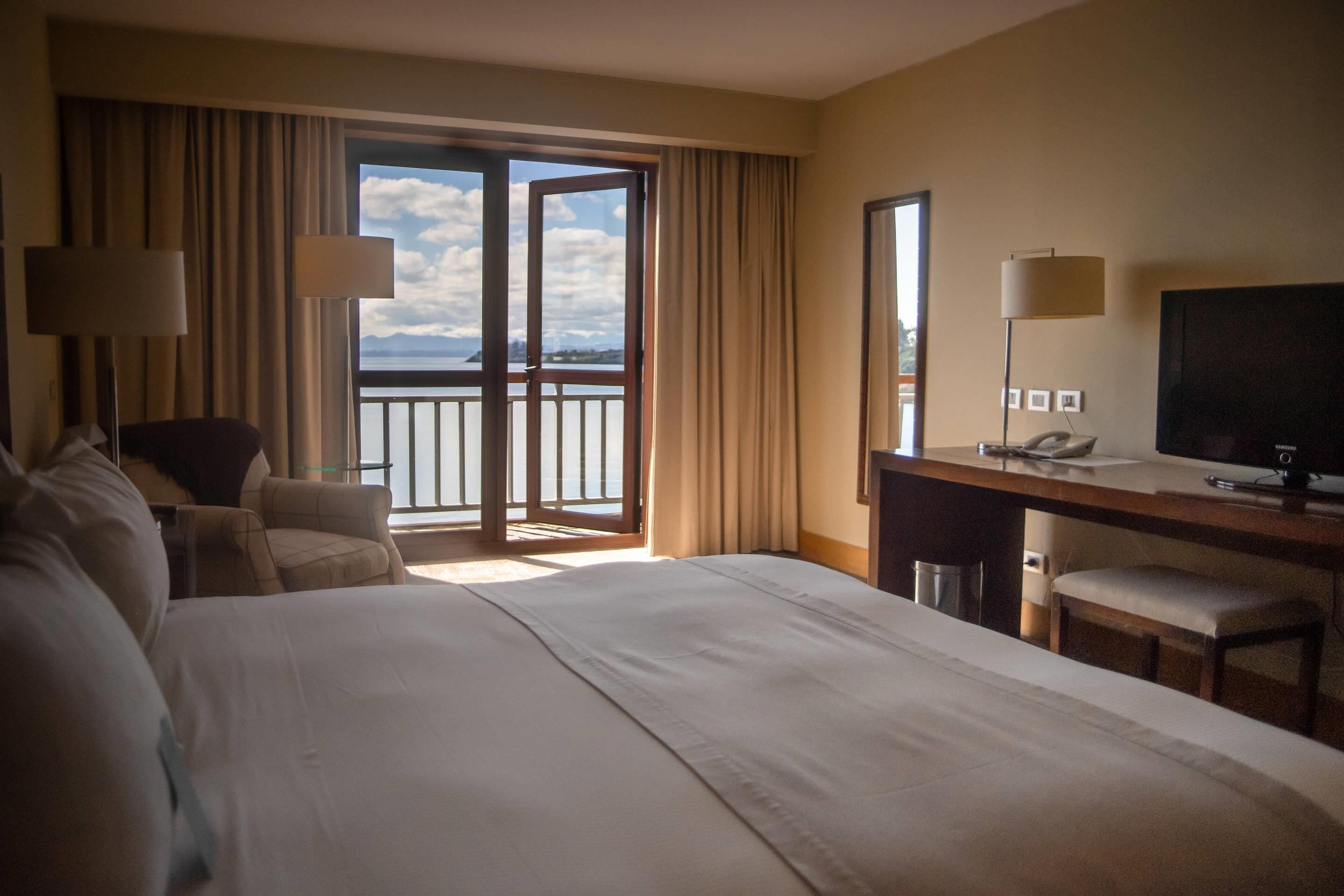 Habitación de hotel con una cama grande, un escritorio con silla, televisión y vistas al exterior a través de una puerta corredera.