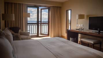 A hotel room with a large bed, a desk with a chair, a television, and a view of the outdoors through a sliding door.