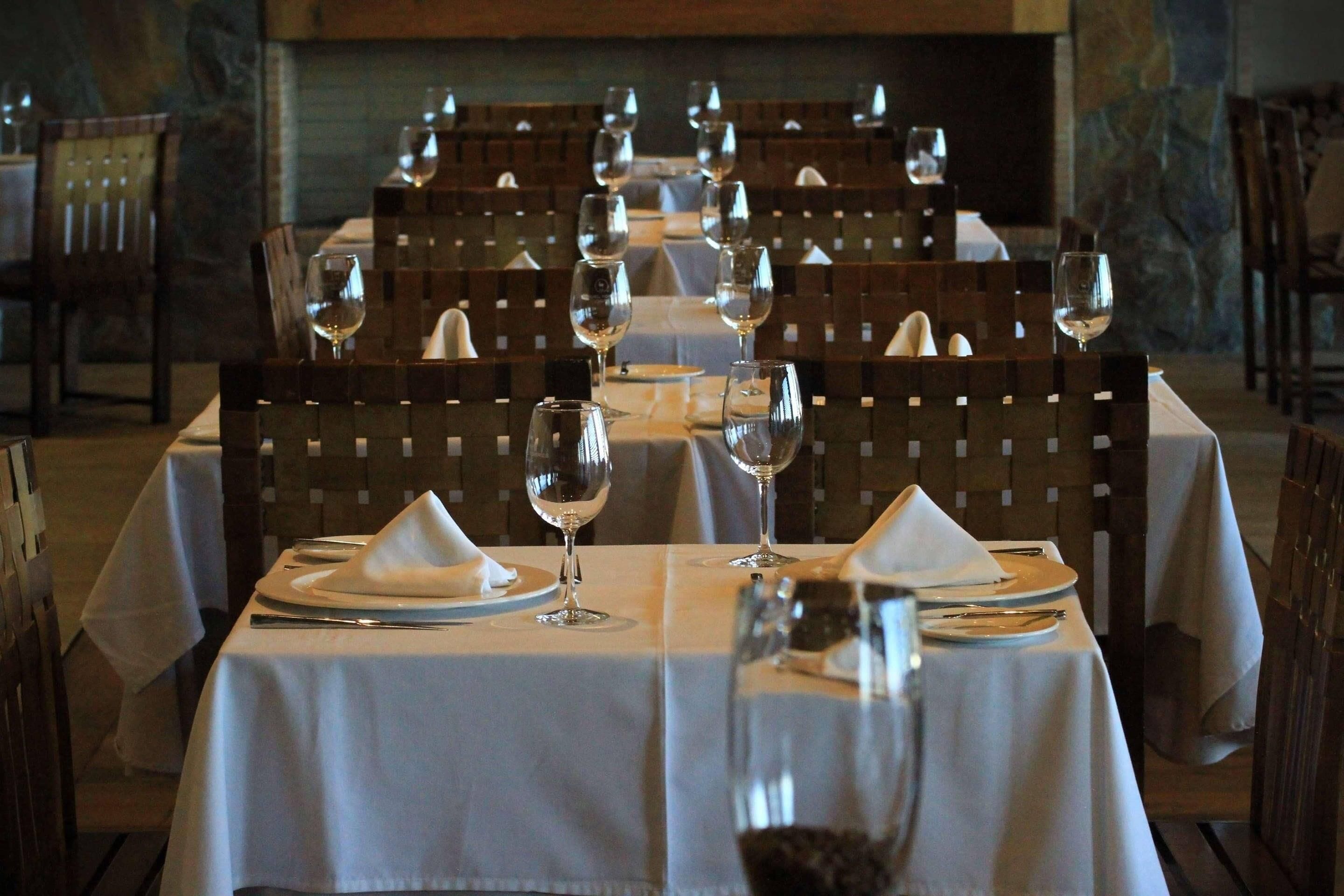 A restaurant with tables set for dining, featuring white tablecloths, wine glasses, and neatly arranged cutlery.