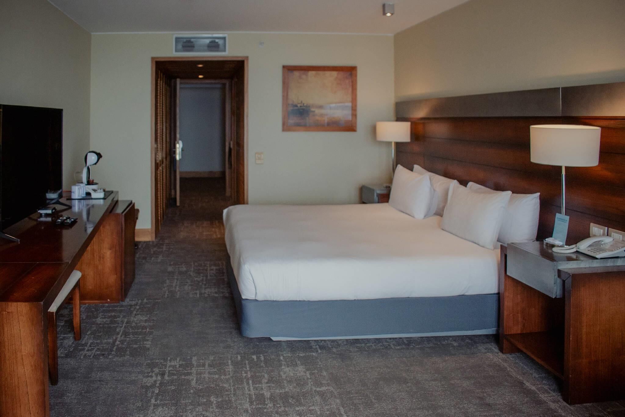 A hotel room with a large bed, a desk with a lamp, a telephone, and a television.