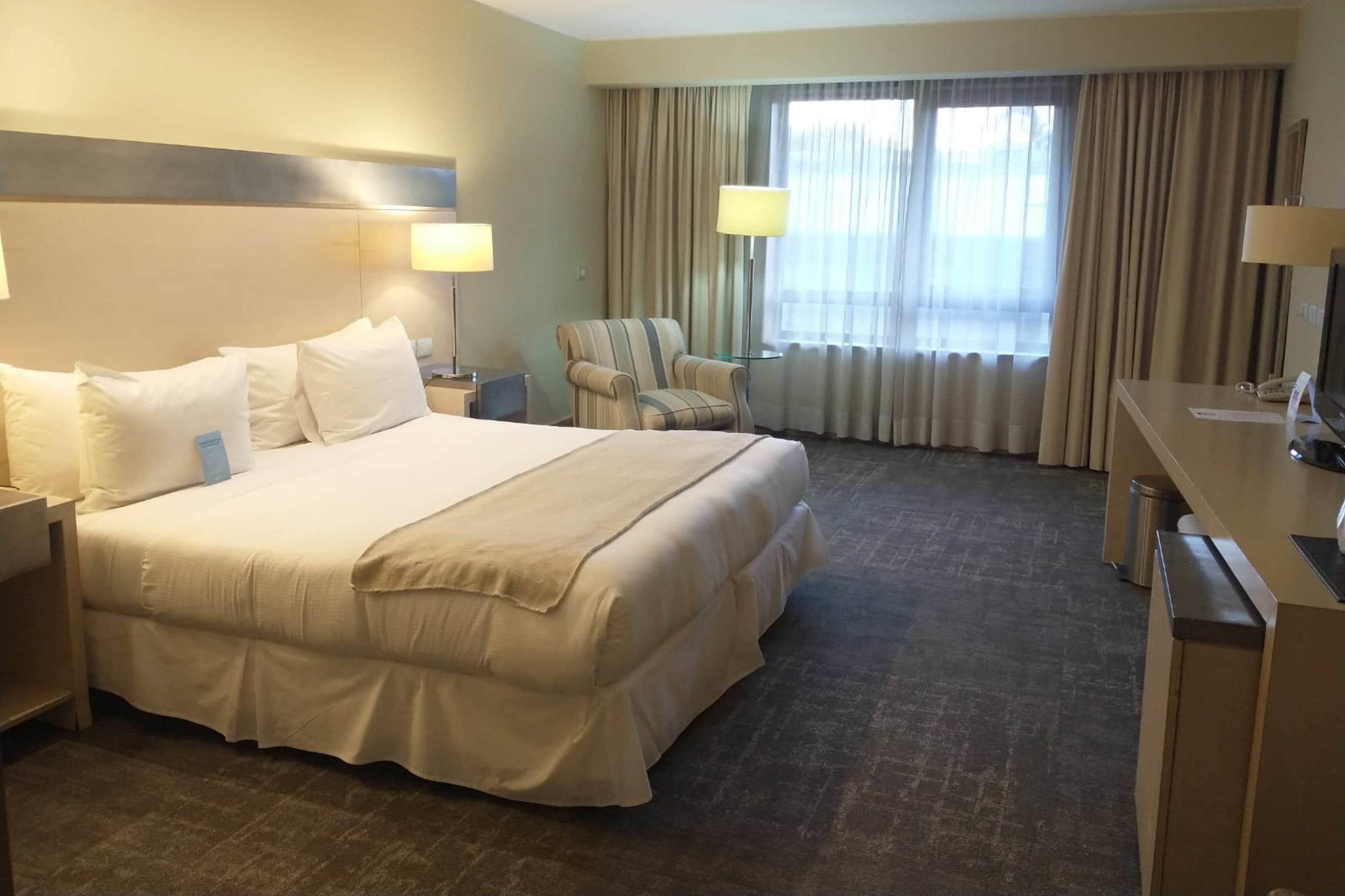 A hotel room with a large bed, two bedside tables, a chair, a desk, and a TV.
