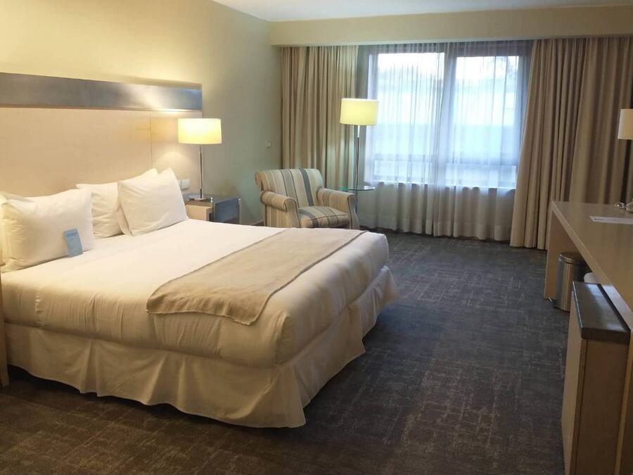 A hotel room with a large bed, two bedside tables, a chair, a desk, and a TV.