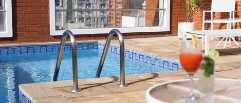 En swimmingpool med metallstegar, ett glasbord med ett glas på och en krukväxt.