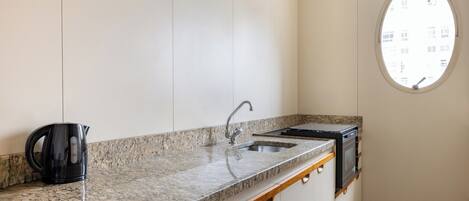 A kitchen with a granite countertop, a black kettle, a sink, and a stove.