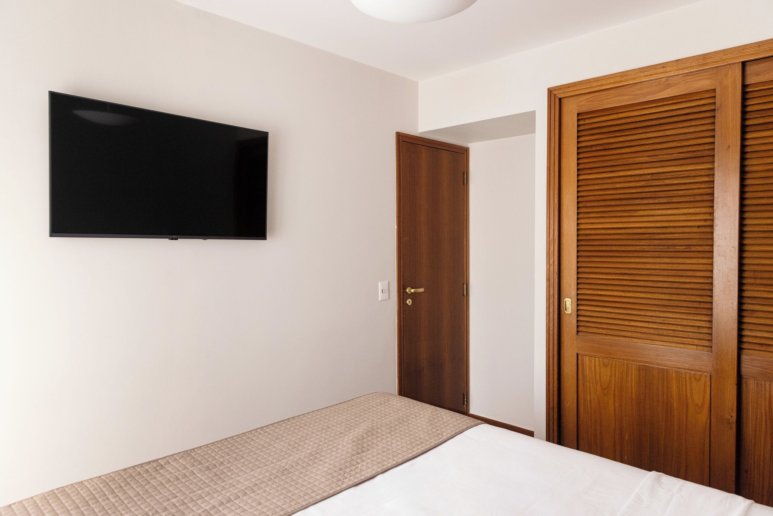 Ein Schlafzimmer mit einem Bett, einem an der Wand montierten Fernseher und einer Holztür.