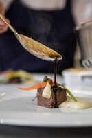 A close-up of a dish with a spoonful of sauce being poured over it.