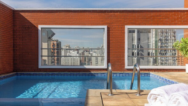 A rooftop pool with a city view, a brick wall, and a window. - Regent Park Hotel (São Paulo)
