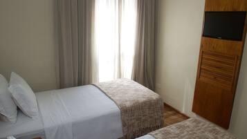 Une chambre d’hôtel avec deux lits, un téléviseur fixé sur un panneau en bois et une fenêtre avec des rideaux.