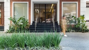 A building entrance with a glass door, steps leading up to it, and a person walking by. - Regent Park Hotel (São Paulo)