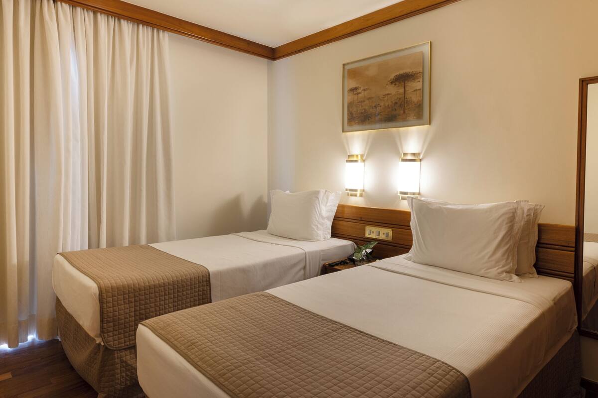 A hotel room with two single beds, a wooden headboard, a painting on the wall, and two bedside lamps.