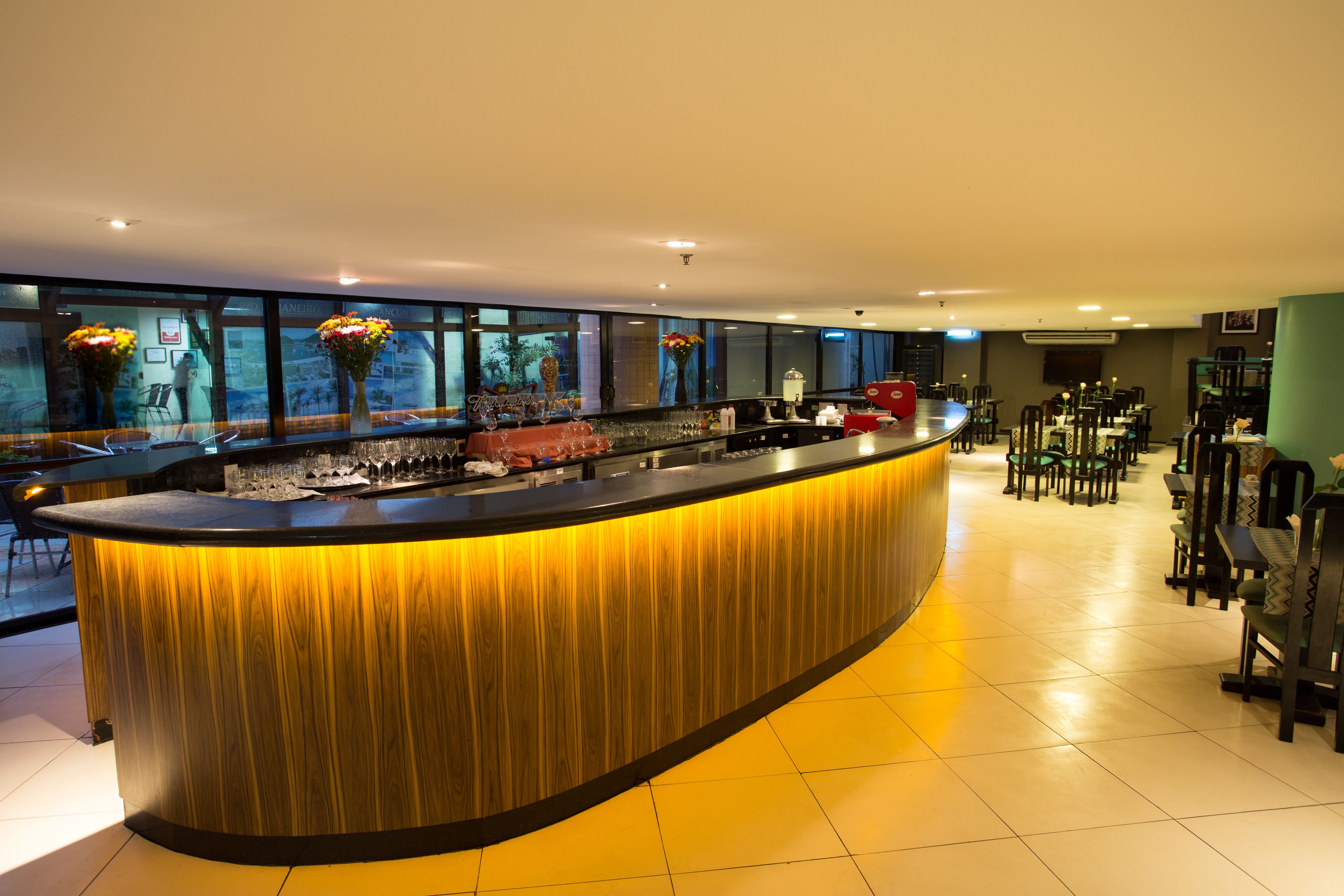 A modern bar area with a curved counter, large windows, and a seating area with tables and chairs.