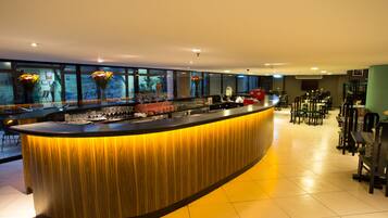 A modern bar area with a curved counter, large windows, and a seating area with tables and chairs.