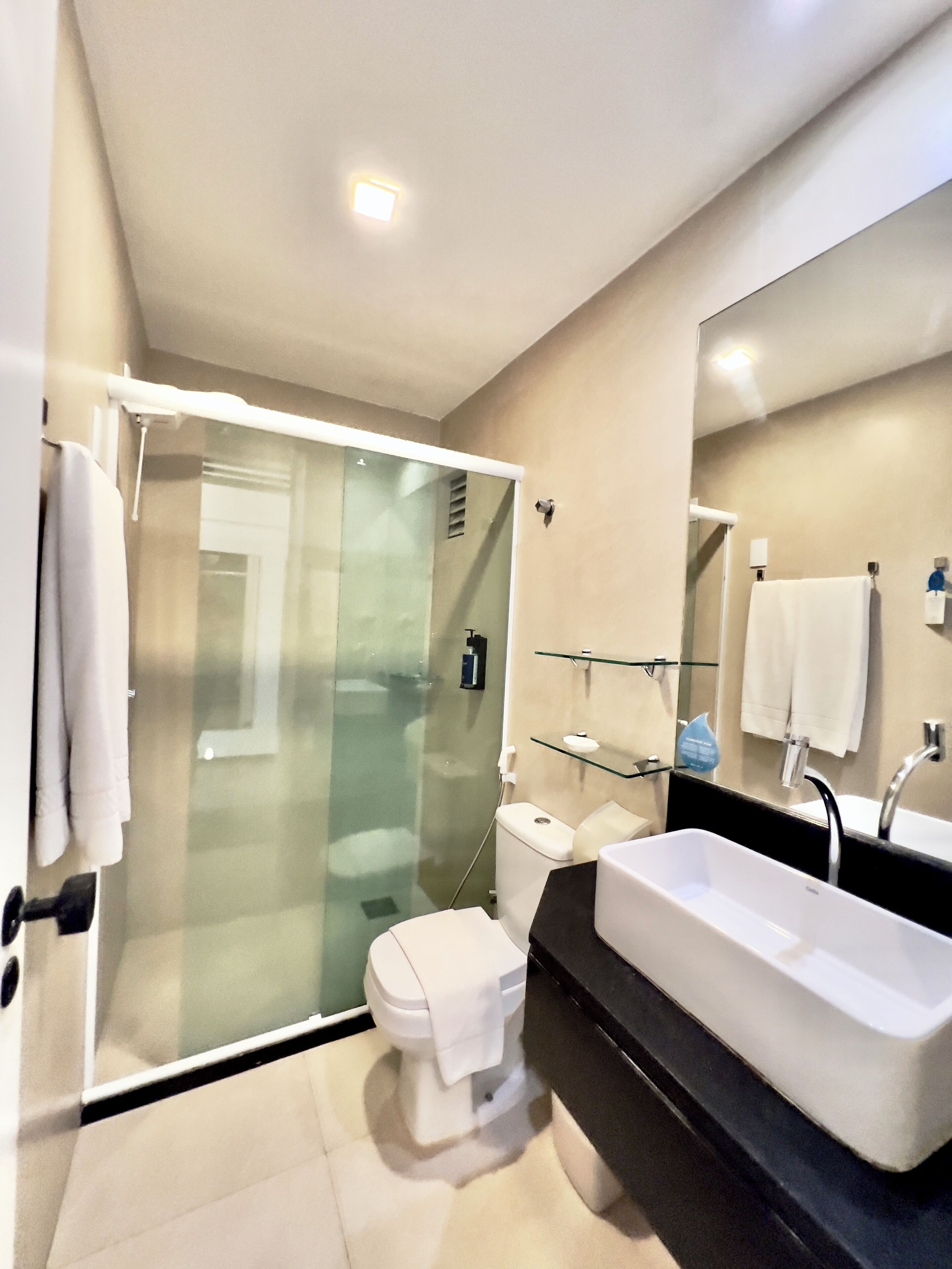 Een moderne badkamer met een glazen douchecabine, een wit toilet, een groot wit wastafelmeubel en een spiegel boven het wastafelmeubel.
