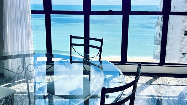 A round glass table with chairs in a room with large windows overlooking the ocean. - Hotel Brasil Tropical (Fortaleza)
