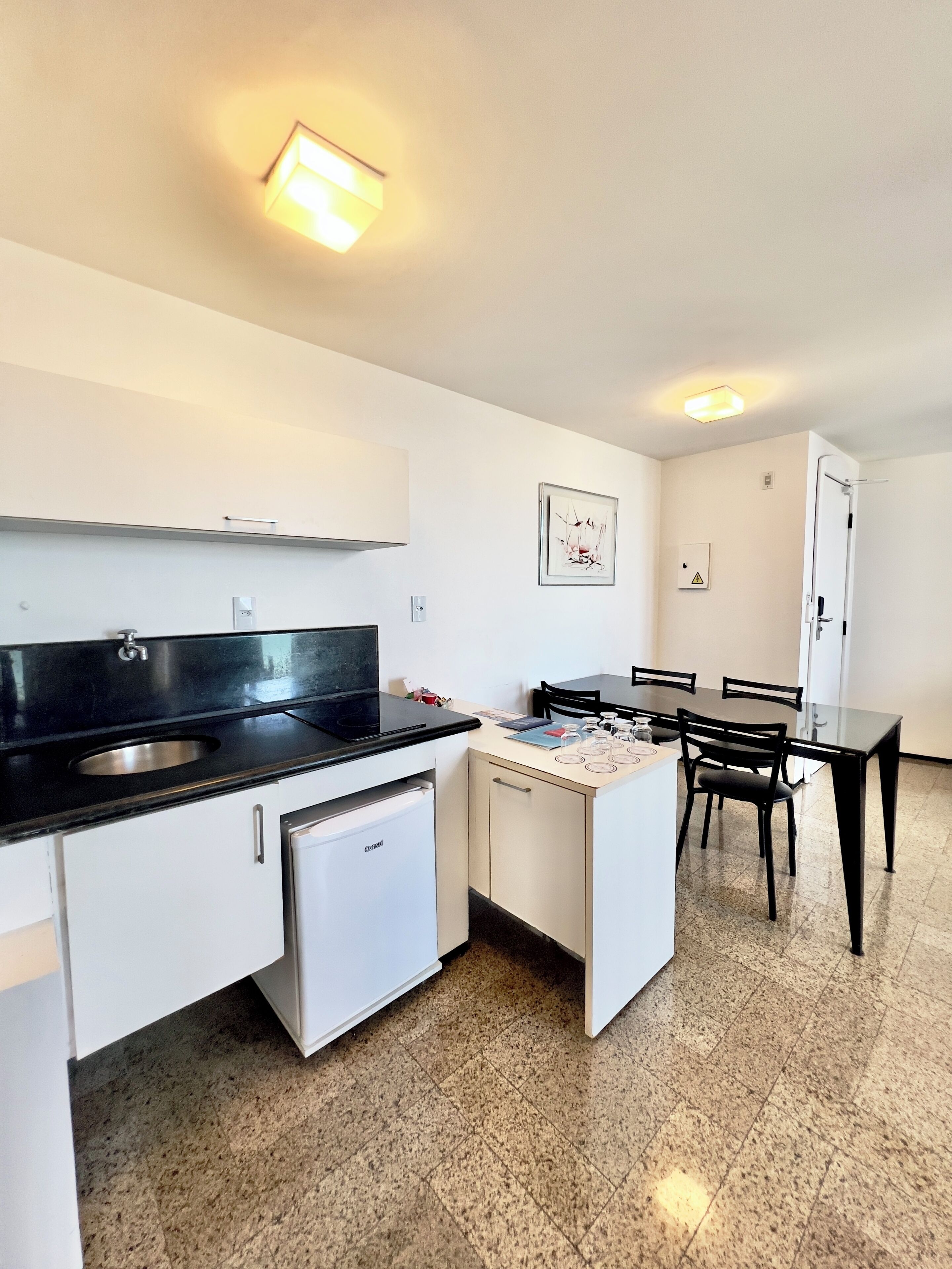 A compact kitchen with a black countertop, white cabinets, a small refrigerator, and a dining area with a table and chairs.