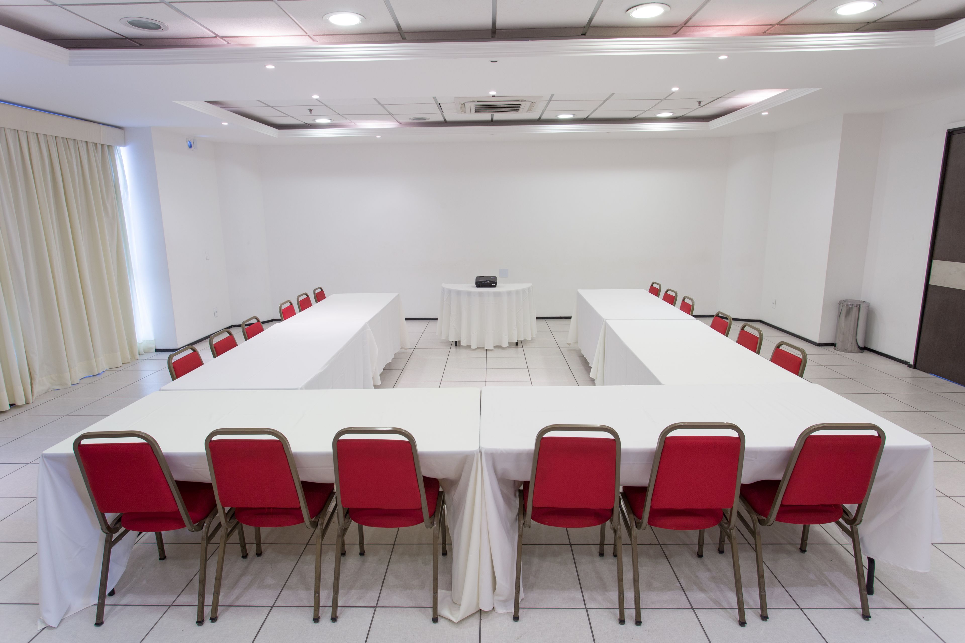Ein Konferenzraum mit einem langen Tisch, roten Stühlen und einer weißen Tischdecke.
