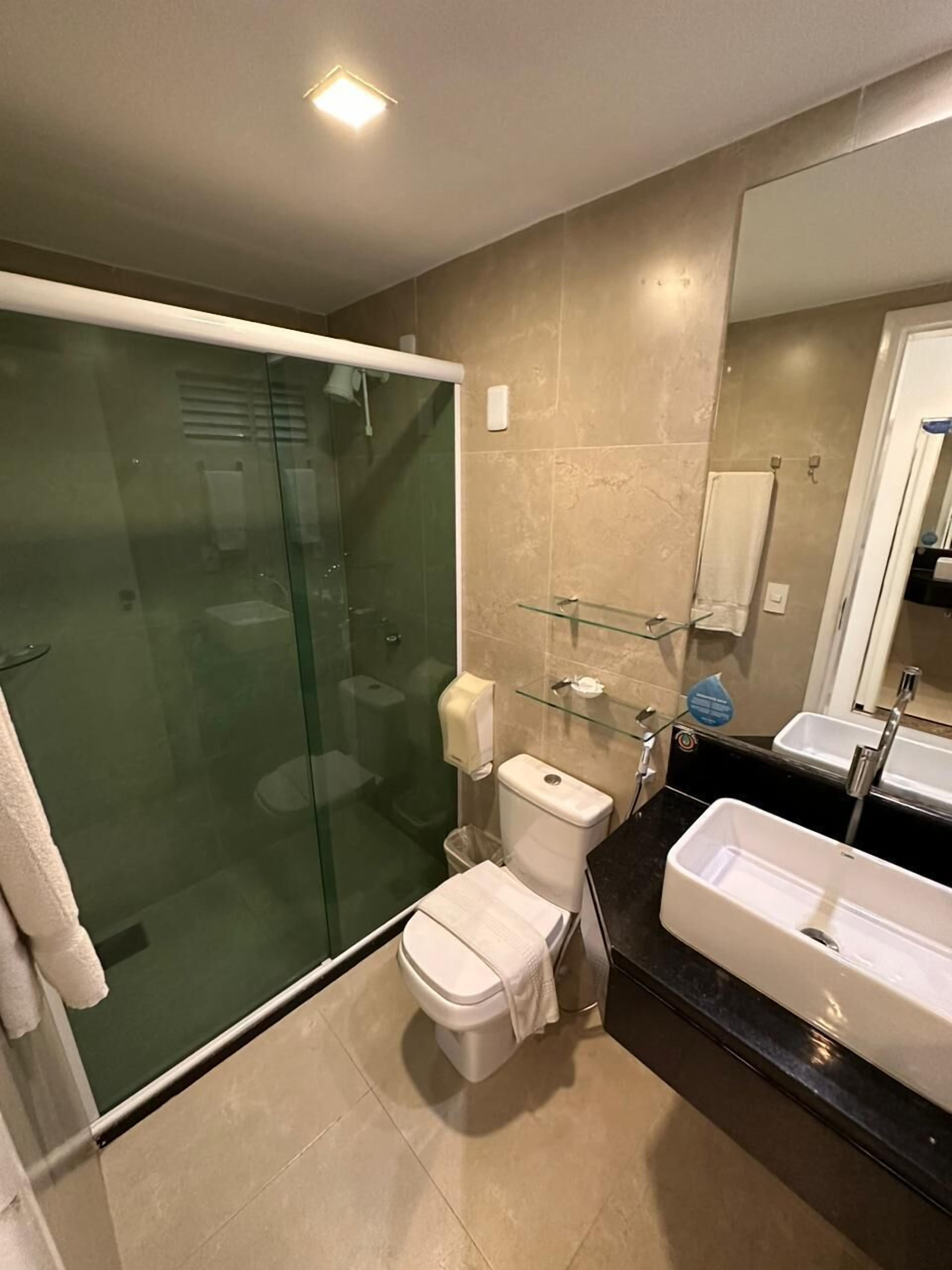Un baño moderno con ducha envuelta en vidrio, un inodoro, un lavabo y un espejo grande.
