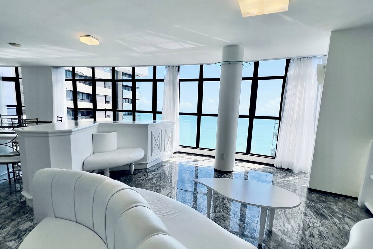 Un moderno vestíbulo de hotel con piso de mármol, sofás blancos, una pequeña mesa redonda y amplios ventanales que ofrecen vistas de la ciudad.