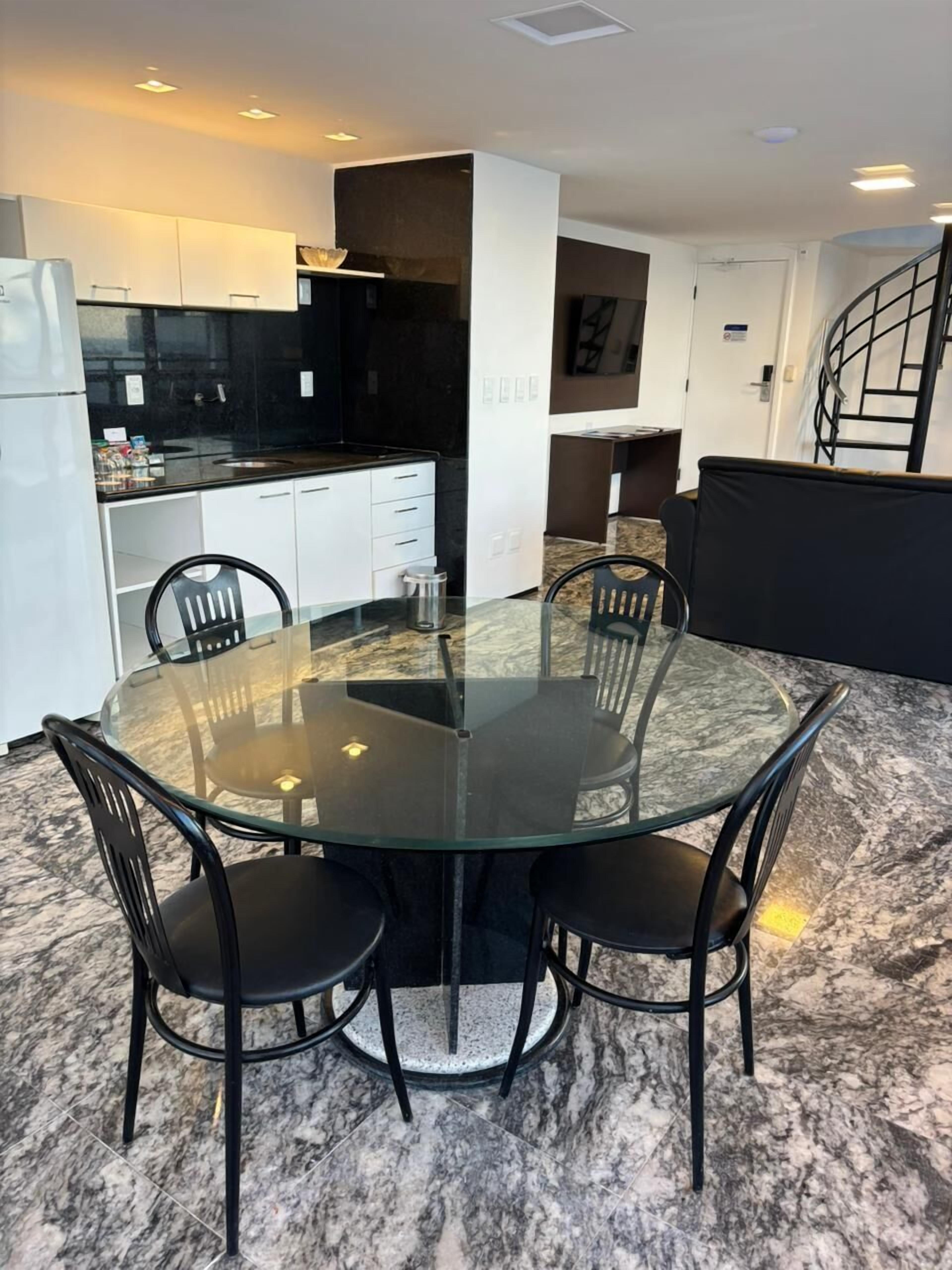 Une cuisine moderne avec un plan de travail noir, des meubles blancs et une table à manger en verre entourée de chaises.