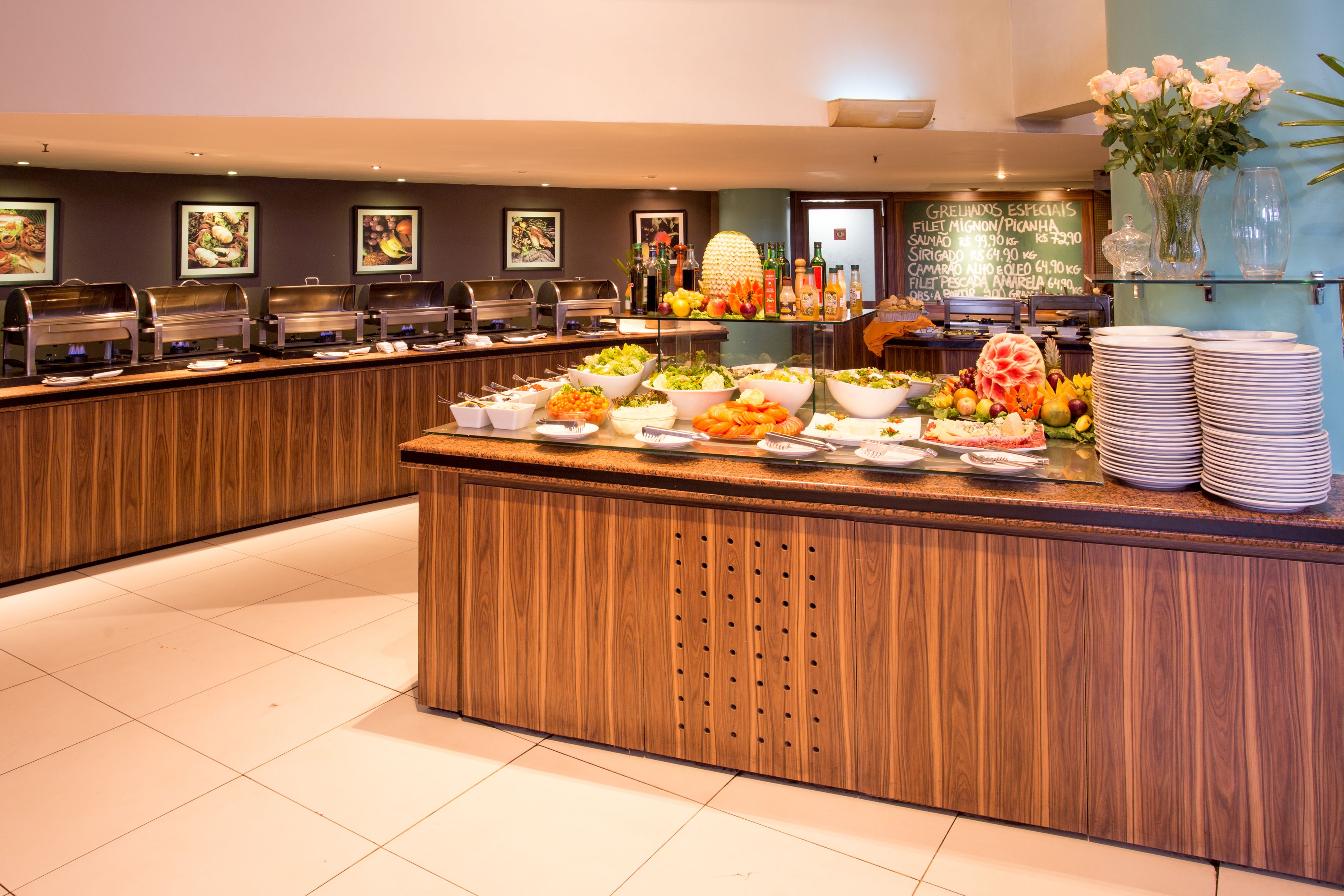 A buffet setup with various food items and beverages, a wooden counter, and a wall with framed pictures.
