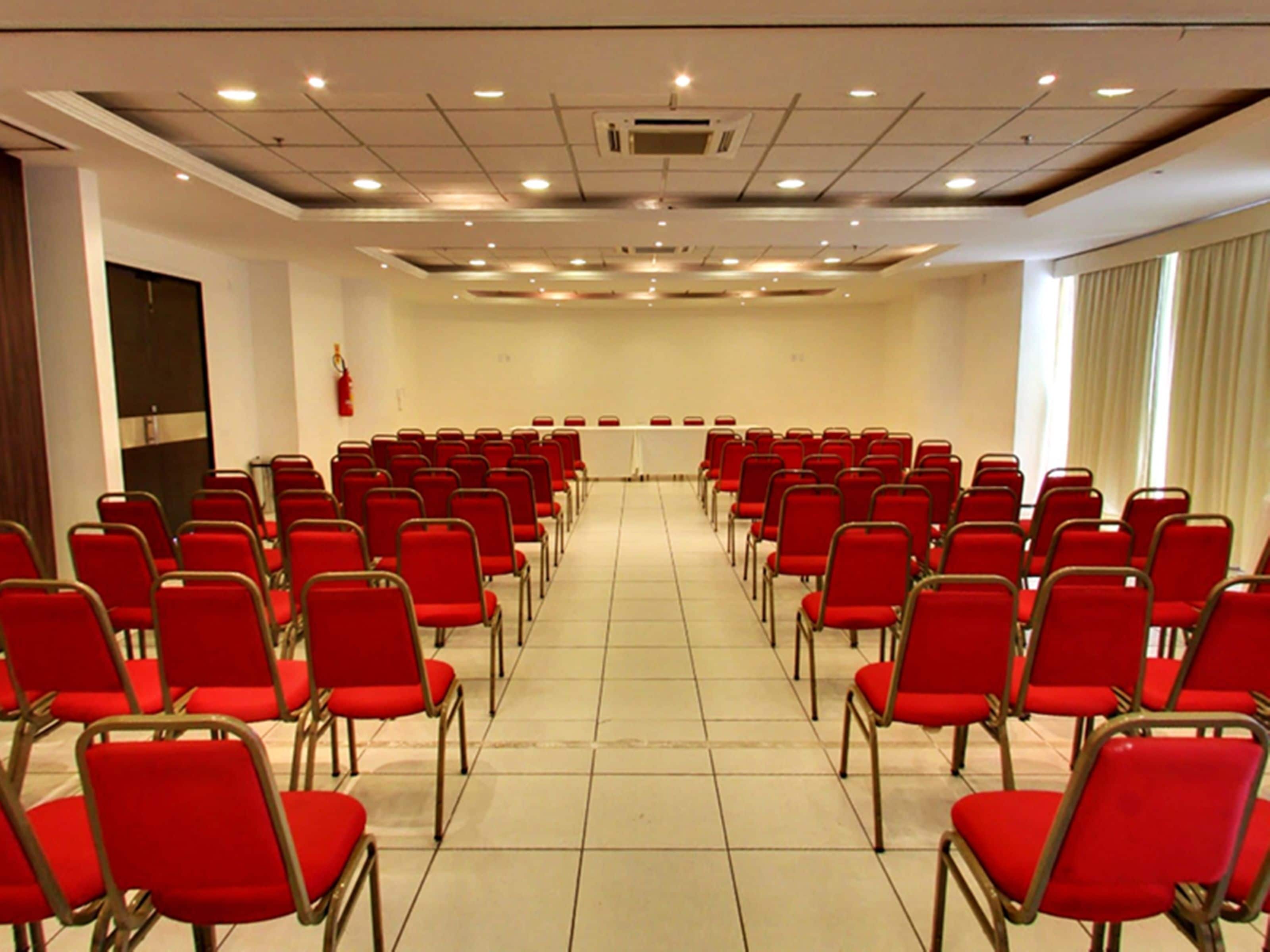 Un salón de conferencias con filas de sillas rojas y una mesa blanca al frente.
