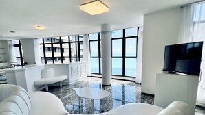 A modern living room with a white sofa, a small table, and a television. The room has large windows and a view of the sea. - Hotel Brasil Tropical (Fortaleza)