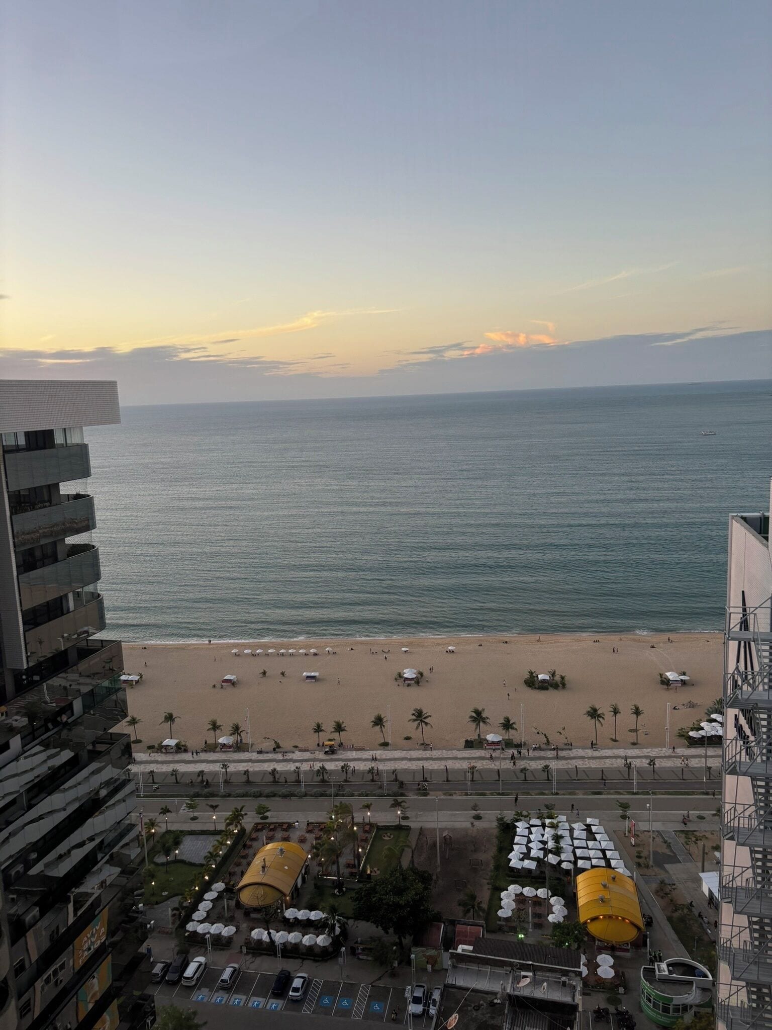 A beach view from a high-rise building with a parking area and outdoor seating.