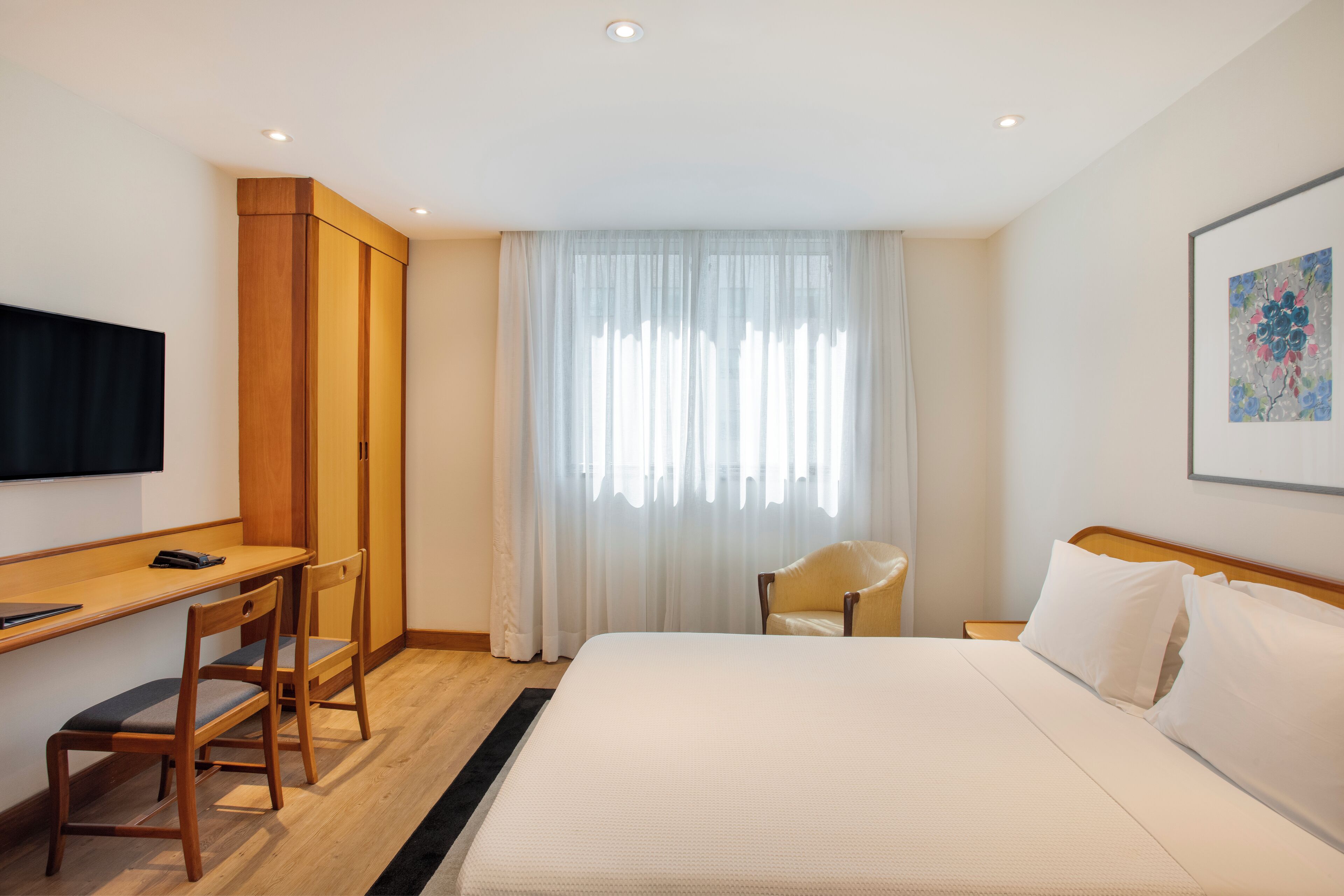 Una habitación de hotel con una cama, un escritorio con silla, un televisor y un armario.