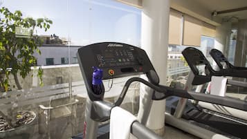 A treadmill in a gym with a control panel, a water bottle, and a view of buildings outside.