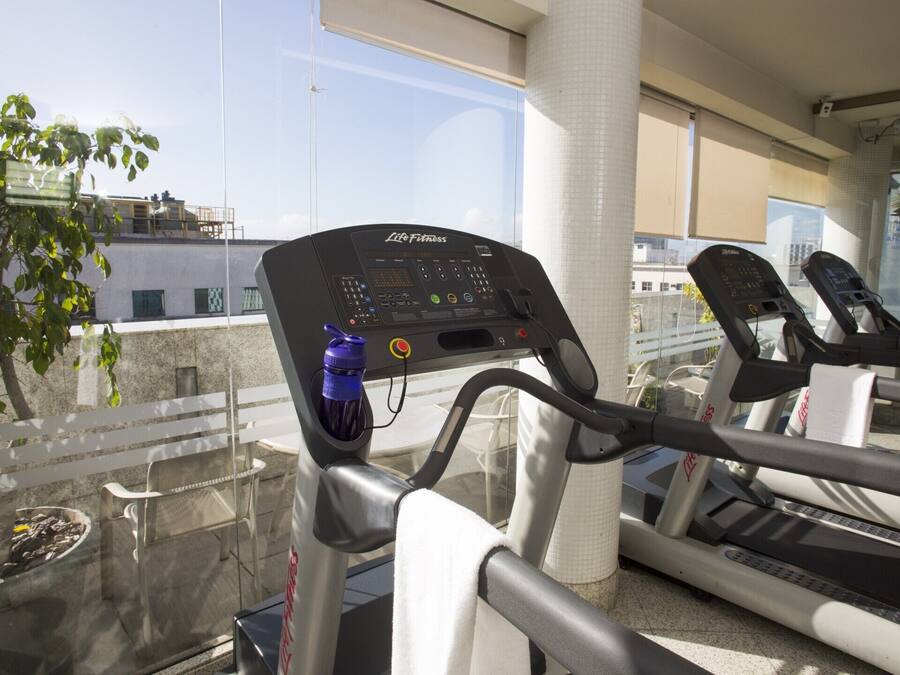 A treadmill in a gym with a control panel, a water bottle, and a view of buildings outside.