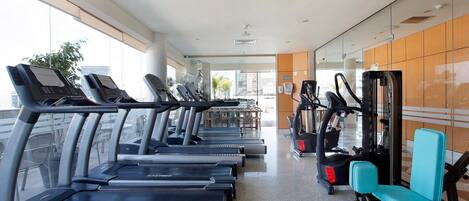 Un gimnasio con cintas de correr, elípticas y una máquina de remo.