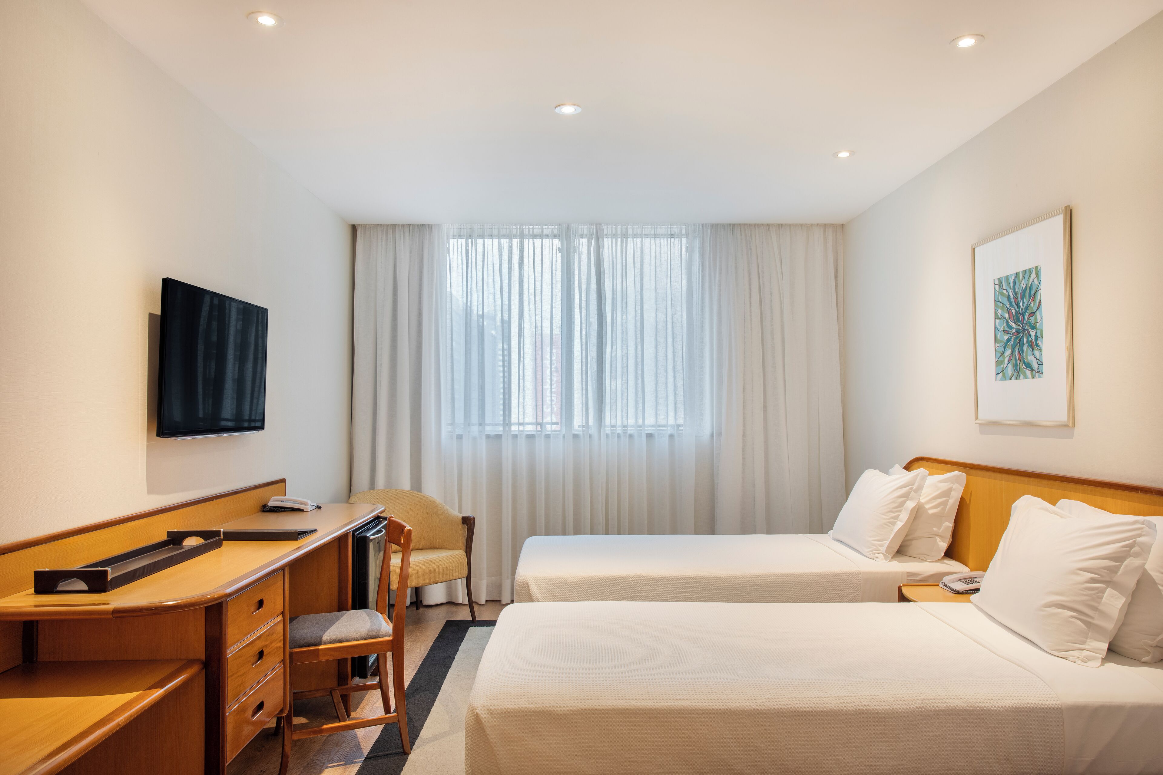 A hotel room with two beds, a desk, a chair, a television, and a window with curtains.