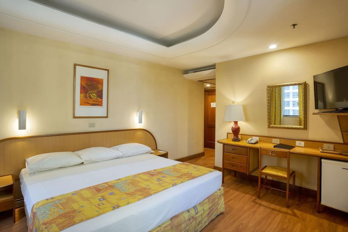 Een hotelkamer met een bed, bureau, stoel, televisie en kunst aan de muur.