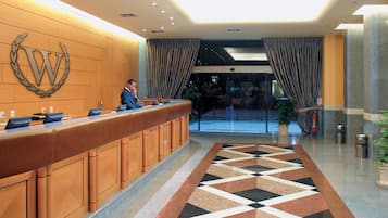 Zona de recepción de un hotel con un mostrador de madera, un gran emblema en la pared y una alfombra estampada.