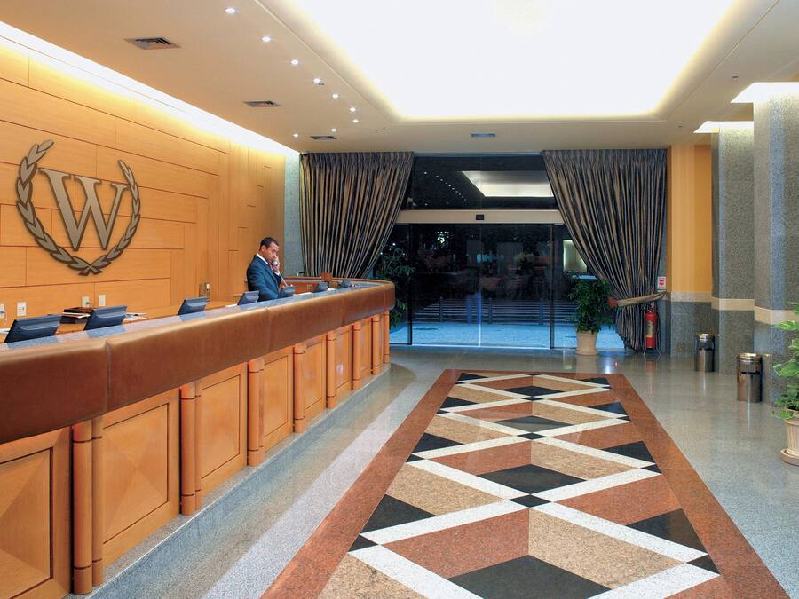 Zona de recepción de un hotel con un mostrador de madera, un gran emblema en la pared y una alfombra estampada.