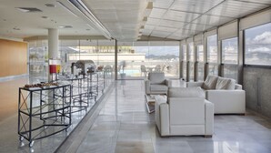 A spacious lounge area with a long counter, white sofas, and a view of the city and mountains through large windows. - Windsor Guanabara Hotel (Rio de Janeiro)