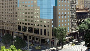 A modern high-rise building with a glass facade, multiple floors, and a prominent entrance at the base. - Windsor Guanabara Hotel (Rio de Janeiro)